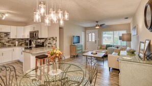A modern kitchen with white cabinets, a granite countertop, and a dining area with a glass table and metal chairs. - 28 Solano (St. Augustine)