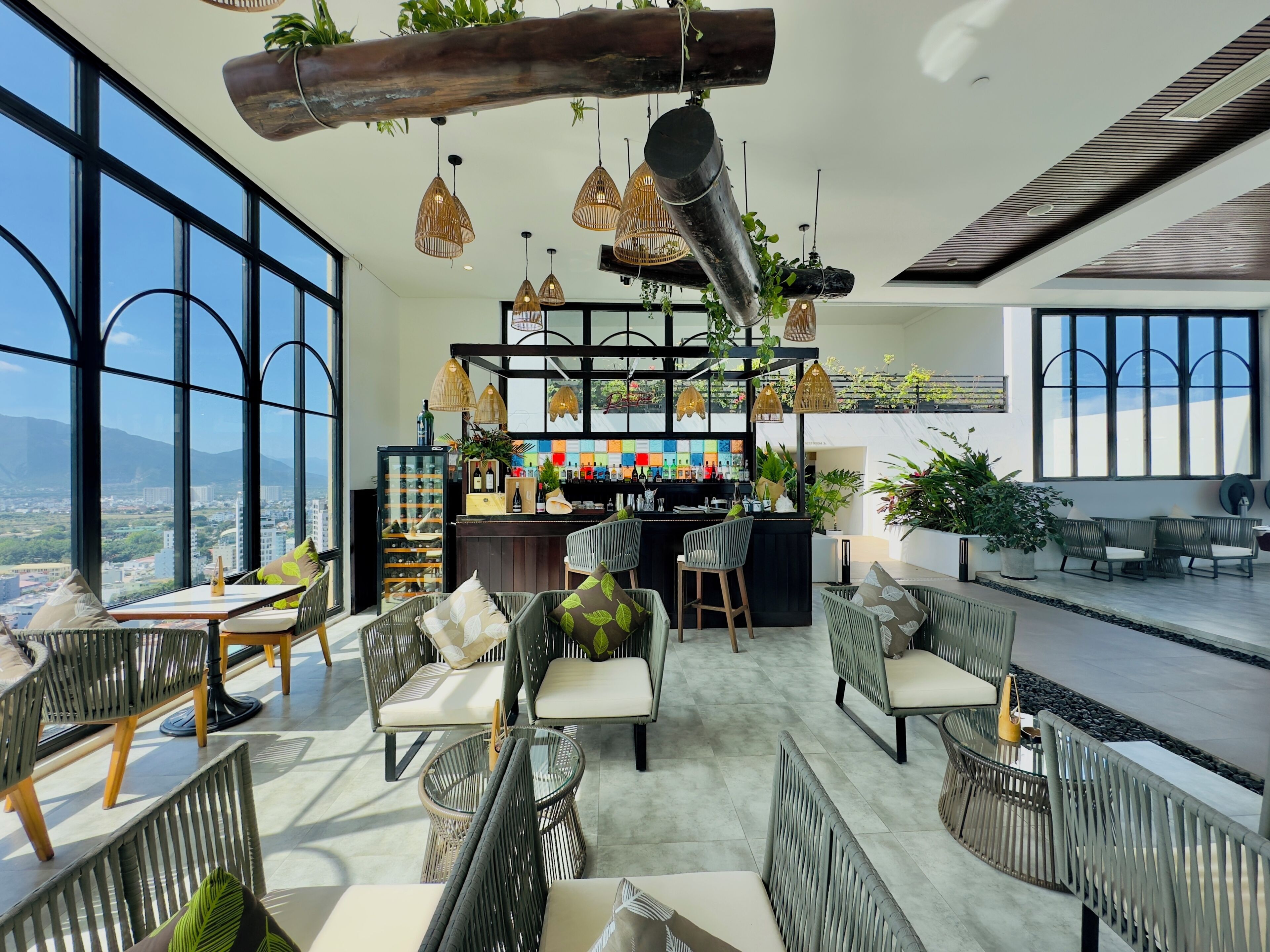 A rooftop bar with wicker furniture, a bar counter, and hanging pendant lights.