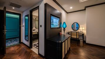 A modern hotel lobby with a wooden herringbone floor, a black console table, a flat-screen TV mounted on a wall, and a teal door.