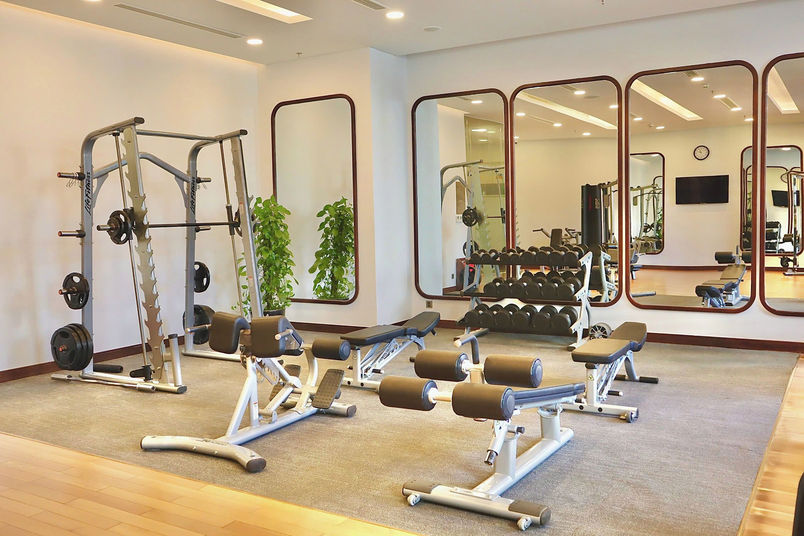 A gym with weightlifting equipment, mirrors, and a clock on the wall.