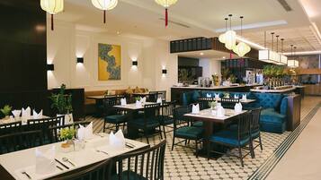 Un restaurante con mesas dispuestas para comer, una zona de bar y un área de estar con sofás acolchados.