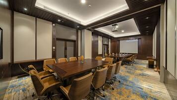 A conference room with a large wooden table, multiple chairs, and a carpeted floor.