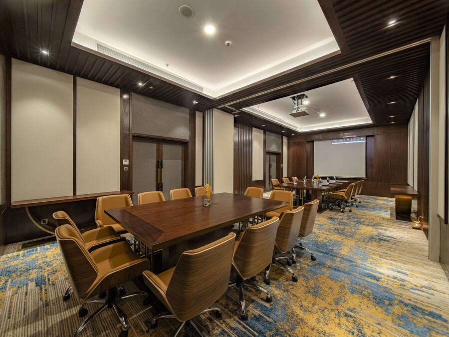 A conference room with a large wooden table, multiple chairs, and a carpeted floor.