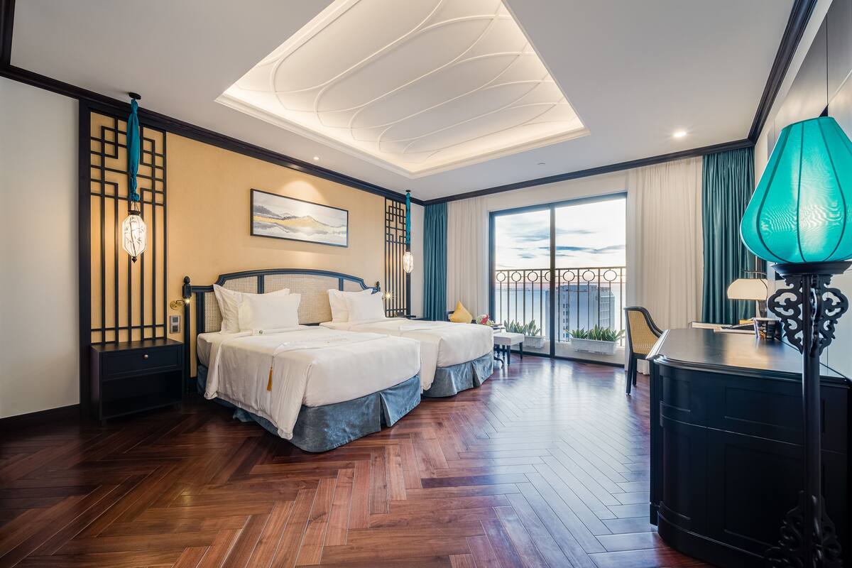 Une chambre d’hôtel avec deux lits, un bureau, un balcon avec vue et un design moderne au niveau du plafond.