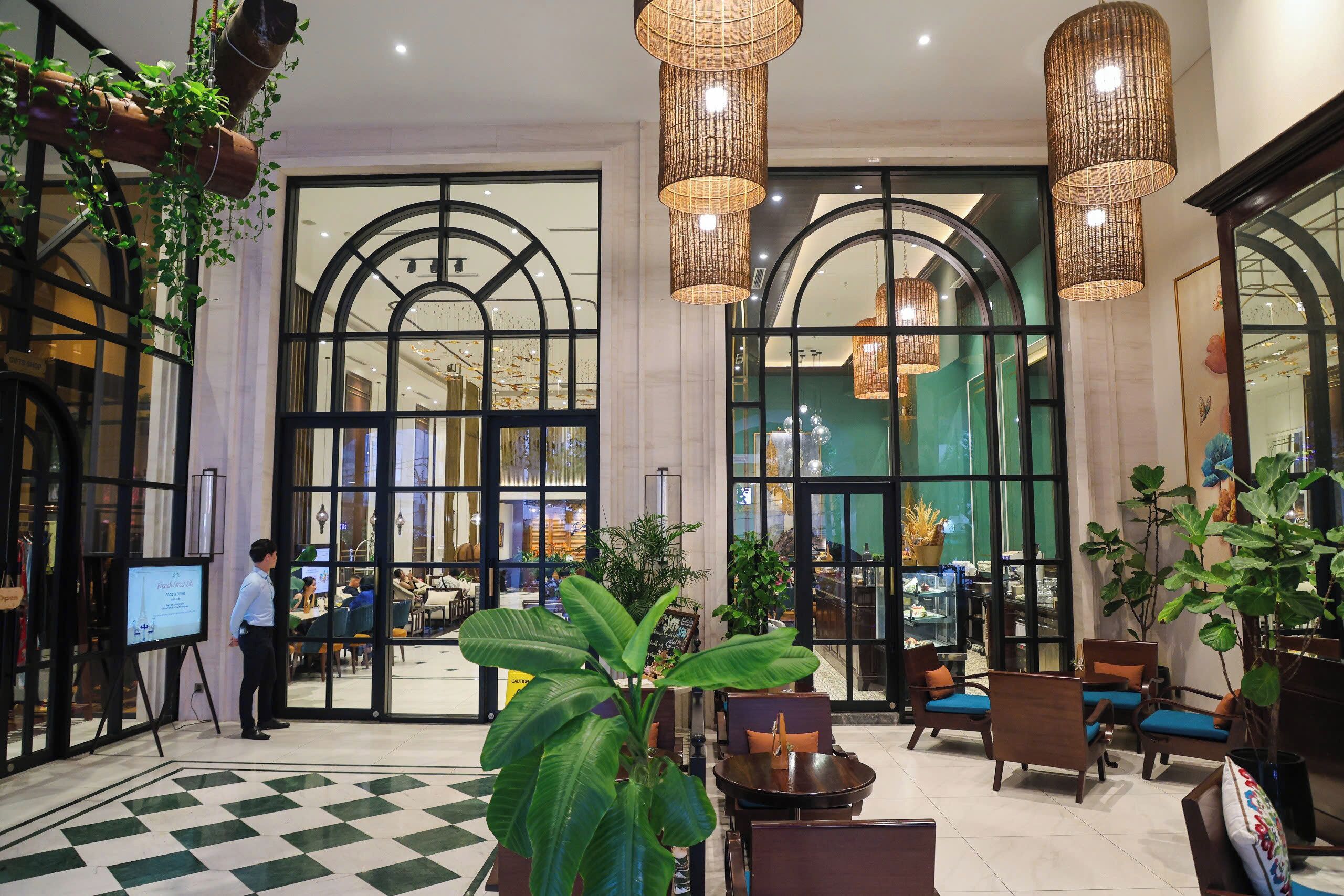 A hotel lobby with large arched windows, hanging wicker lamps, and a checkered floor pattern.