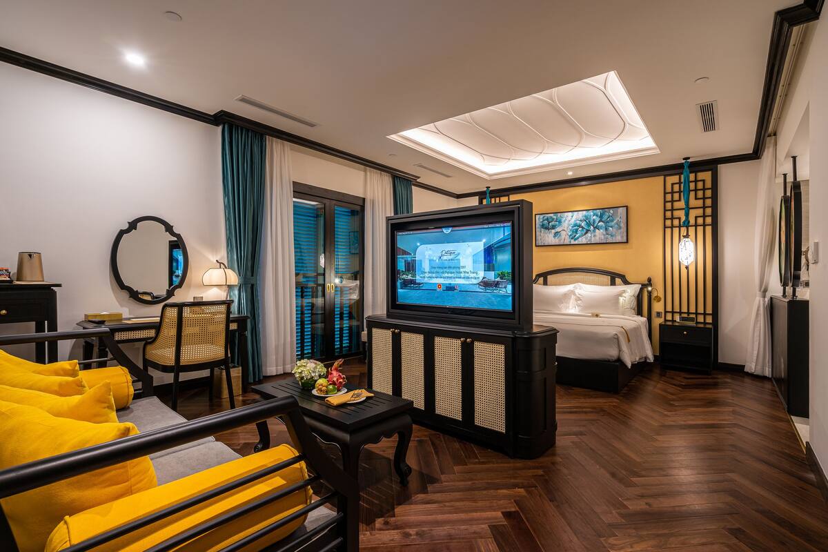Une chambre d’hôtel comprenant un lit, une télévision, un bureau avec une chaise et un canapé avec des coussins jaunes.