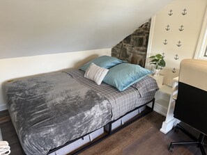A bedroom with a bed, pillows, a nightstand, a chair, and a wall with anchor decorations.