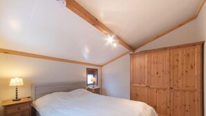 Ein Schlafzimmer mit einem großen Bett, einem Holzschrank, einem Nachttisch mit Lampe und einem kleinen Spiegel.