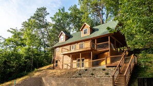 A two-story log cabin with a balcony and a staircase leading to the upper level. - Luxe Pool Cabin Near Dollywood & Top Attractions (Pigeon Forge)