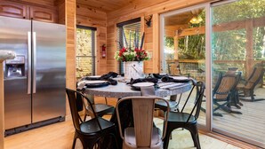 A wooden interior with a round dining table, chairs, a refrigerator, and a window overlooking a deck. - Luxe Pool Cabin Near Dollywood & Top Attractions (Pigeon Forge)