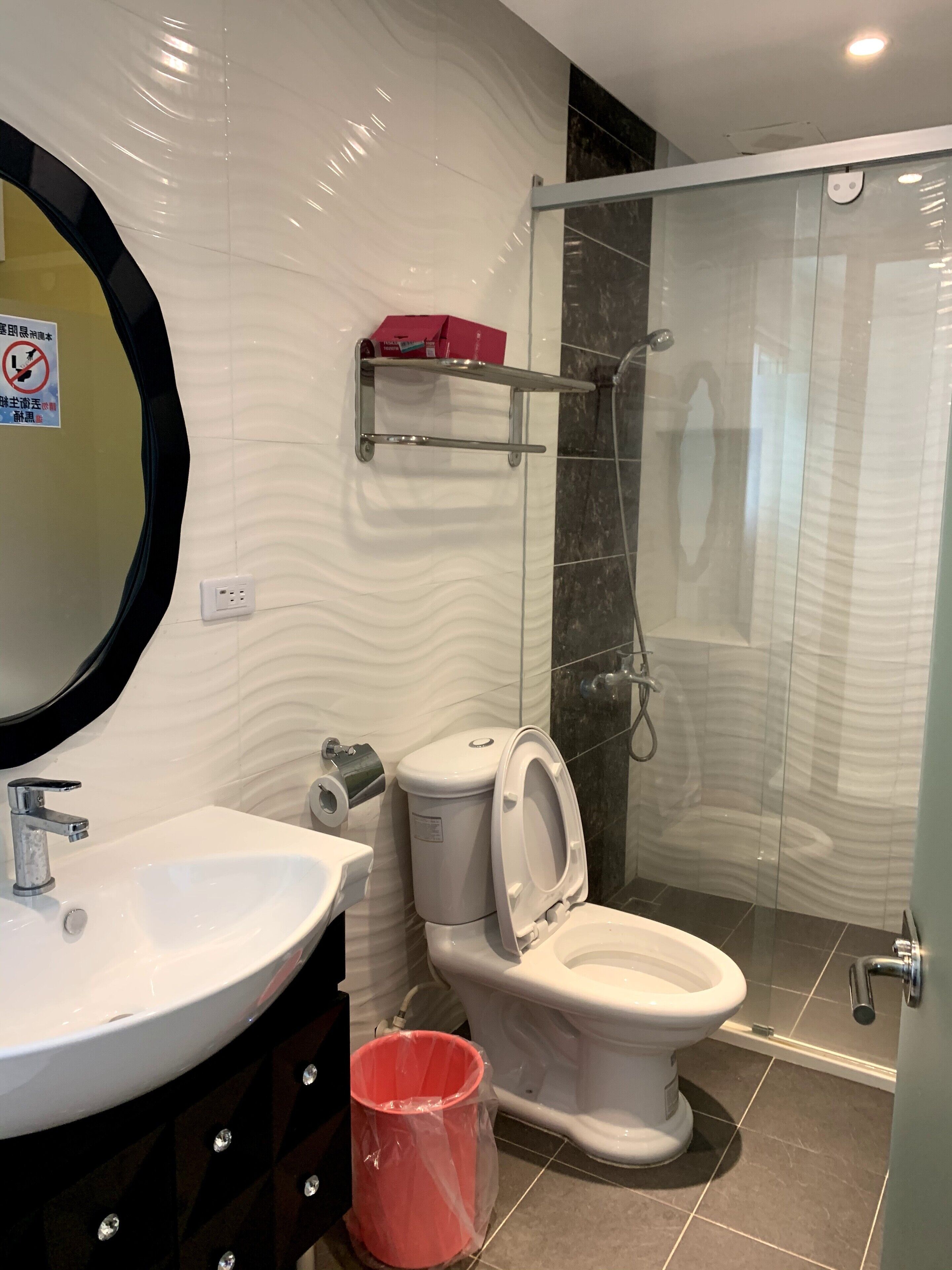 A modern bathroom with a white sink, toilet, and shower. There is a glass shower enclosure and a mirror with a black frame.