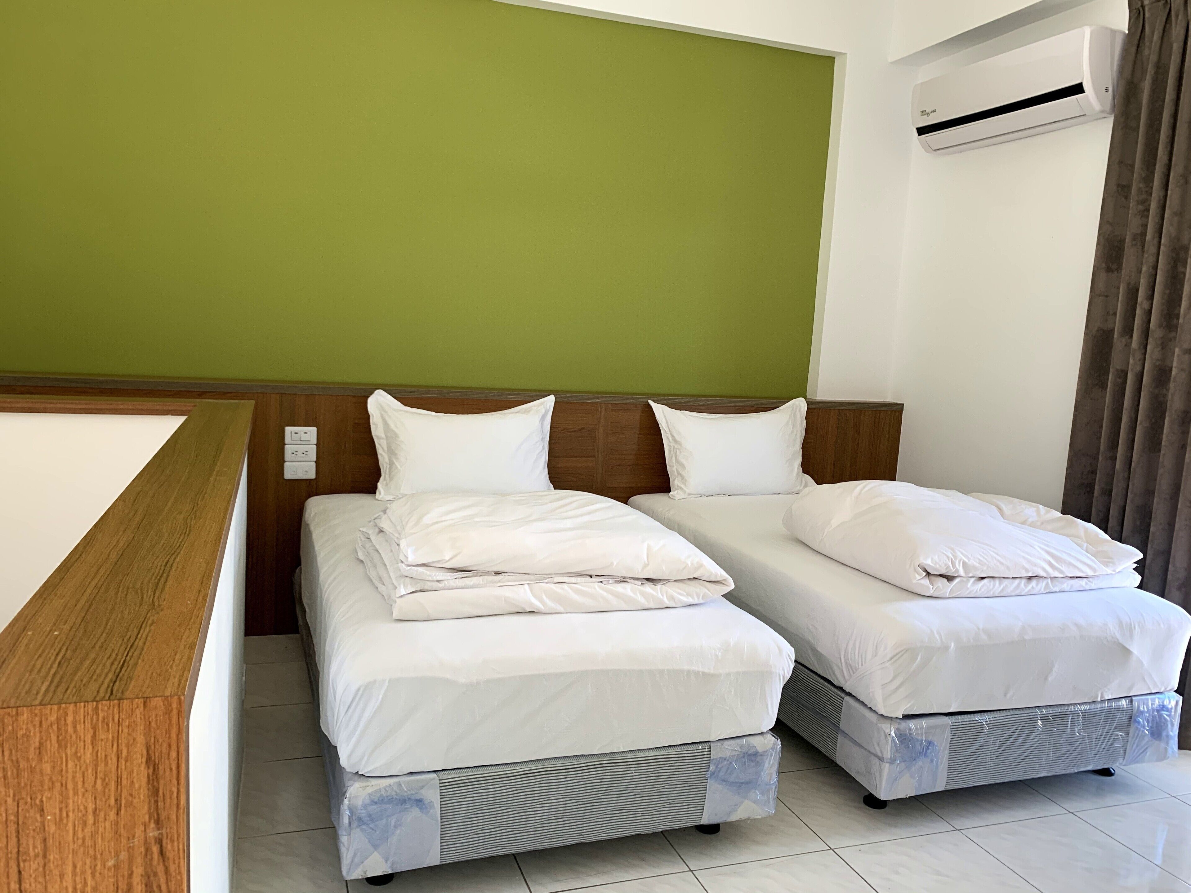 Habitación de hotel con dos camas individuales, cabecero de madera, pared verde y unidad de aire acondicionado.