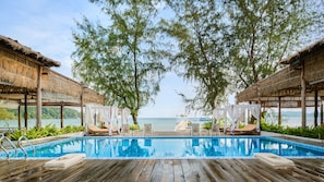 Une terrasse en bois avec une piscine, des chaises longues et une vue sur la mer.