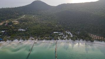 An aerial view of a coastal area with a beach, a pier, and a mountain in the background.