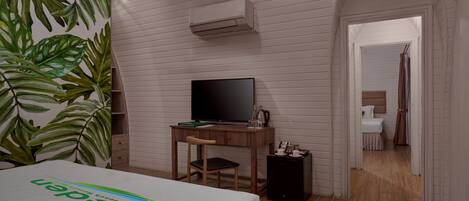 A hotel room with a bed, a desk with a TV, a small cabinet, and a plant.
