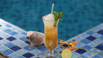 A cocktail glass with ice, garnished with a mint leaf, next to a lime wedge on a tiled surface by a pool.