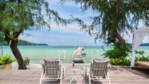 A wooden deck with two chairs and a small table, overlooking a clear blue sea and a distant island. - Eden Beach Resort by EHM (Koh Rong Sanloem)