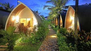 A pathway leading to two dome-shaped accommodations with wooden facades, surrounded by lush greenery and palm trees. - Eden Beach Resort by EHM (Koh Rong Sanloem)