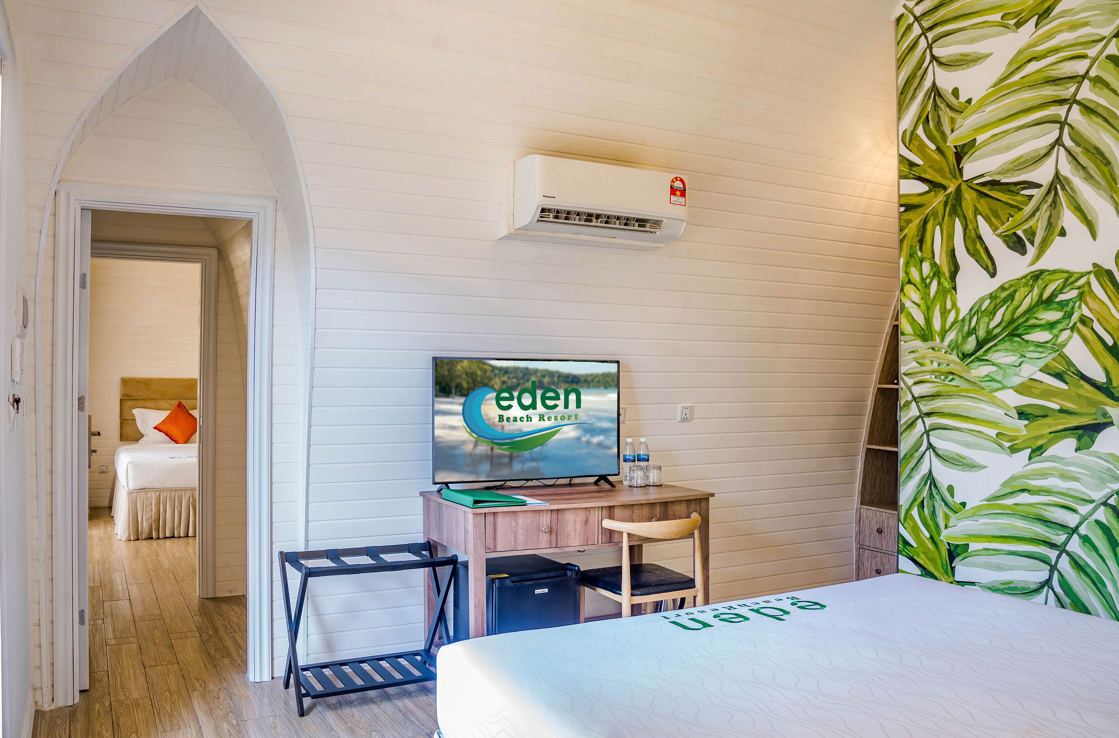 A hotel room with a bed, a desk with a chair, a television, and an air conditioning unit.