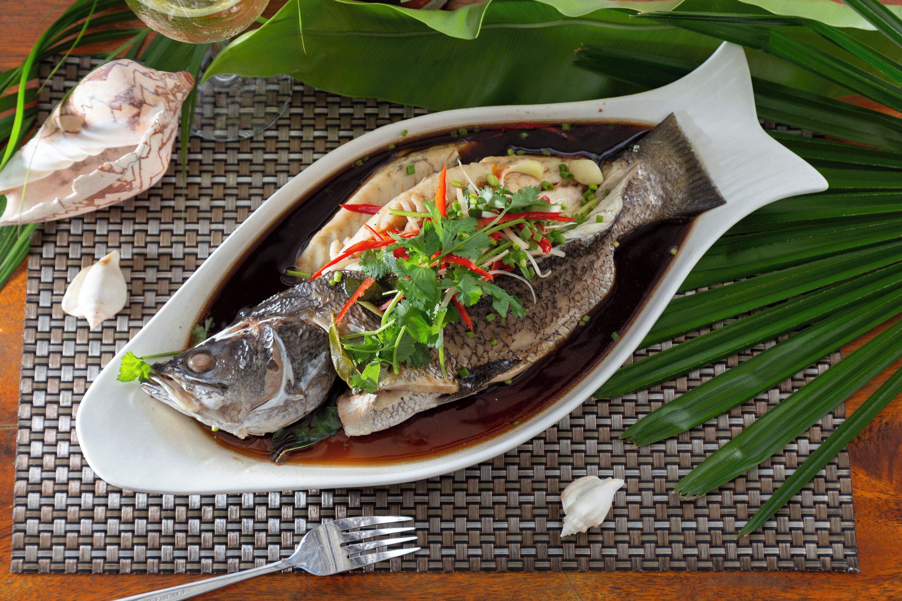 A dish of fish garnished with herbs and vegetables on a white plate.