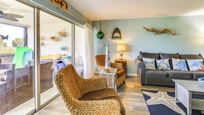 A living room with wicker furniture, a grey sofa with colorful cushions, a starfish rug, and a view through a sliding glass door to an outdoor area. - Beachfront Siesta Key Condo w/ Enclosed Patio (Siesta Key)