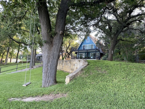 A house with a stone retaining wall, a swing set, and a well-maintained lawn.