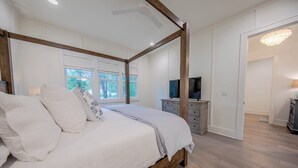 Un lit à baldaquin avec un cadre en bois, un téléviseur posé sur une commode et un lustre dans la pièce.