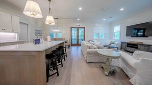 A spacious living area with a large island, white sofas, and a TV mounted on the wall. - 4 BR Grayton Beach, private beach, Tesla charger, 2 pools, tennis, & Pickle ball (Santa Rosa Beach)