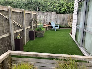 A backyard with artificial grass, a wooden fence, a blue chair, and potted plants.