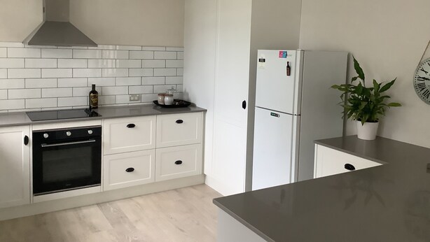 Una cuina moderna amb armaris blancs, forn de sobretaula, campana extractora d'acer inoxidable, nevera blanca i una planta en maceta al taulell.