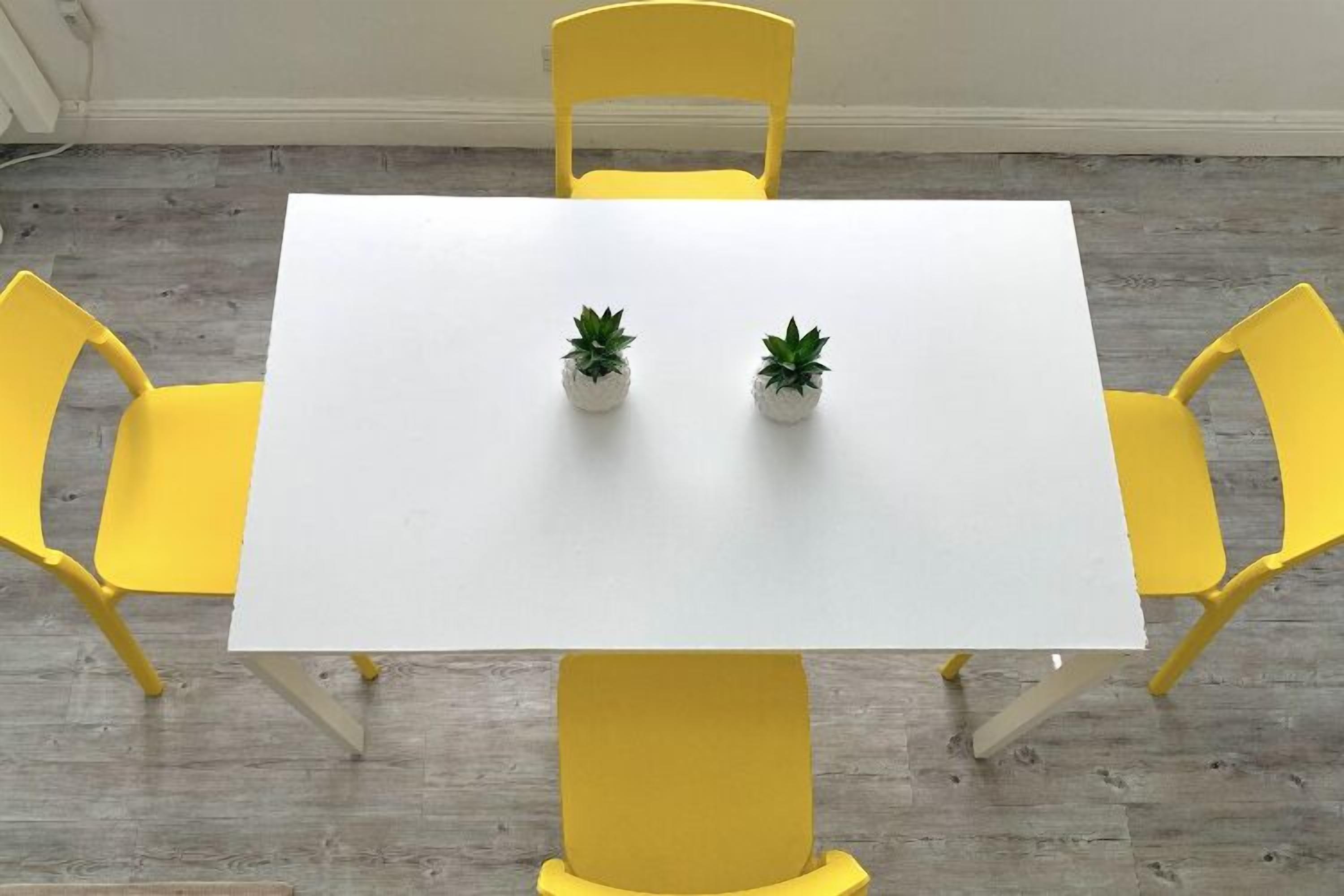 Una mesa blanca con dos plantas en macetas, rodeada de sillas amarillas.
