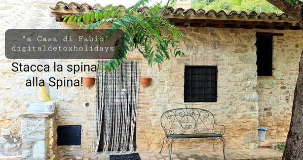 Un edificio de piedra rústico con un banco, una planta colgante y un letrero.