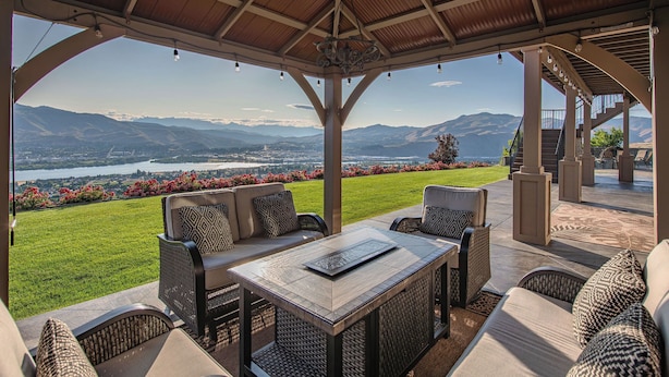 An outdoor patio with a view of a lake and mountains, furnished with wicker chairs and a table. - Riverview Retreat: Incredible Views, Heated Pool, Spa, Theater Room & More! (East Wenatchee)