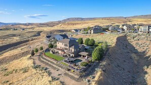 A large, multi-story house with a spacious patio and a swimming pool, surrounded by a hilly landscape. - Riverview Retreat: Incredible Views, Heated Pool, Spa, Theater Room & More! (East Wenatchee)