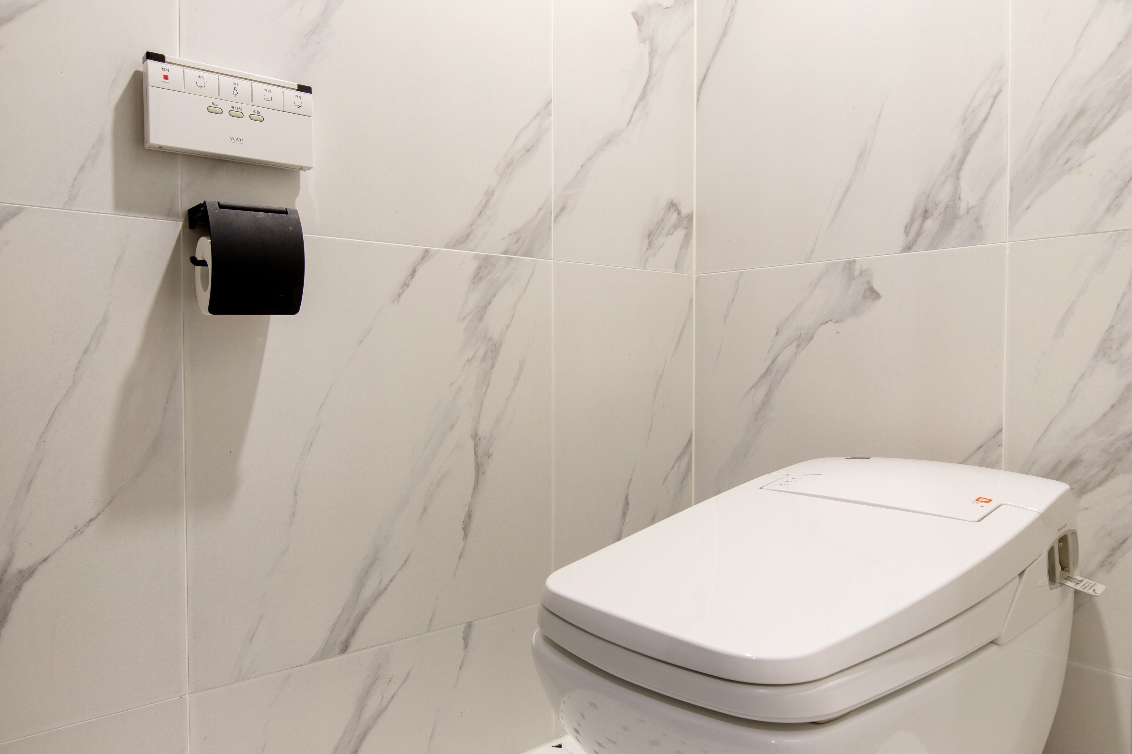 Ein Badezimmer mit Toilette, Papierhandtuchspender und Bedienfeld an der Wand.