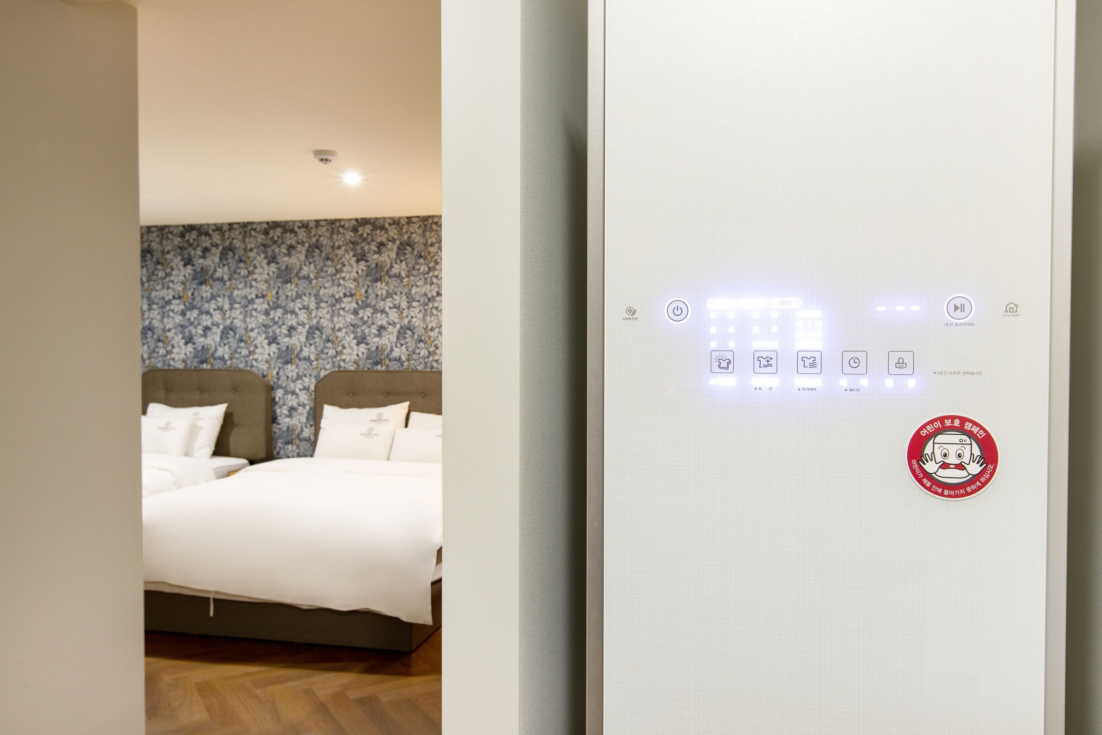 A hotel room with a bed, a control panel with lights, and a floral wallpaper.