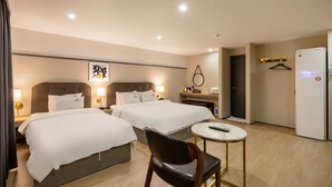 Una habitación de hotel con dos camas, una mesita pequeña, una silla, un refrigerador y una puerta.