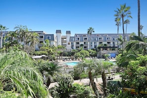 Een resort met een zwembad, omgeven door palmbomen en een meerlaags gebouw met balkons.