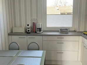 Eine kleine Küche mit Fenster, einer Kaffeemaschine, einem Toaster und einer Waschmaschine.