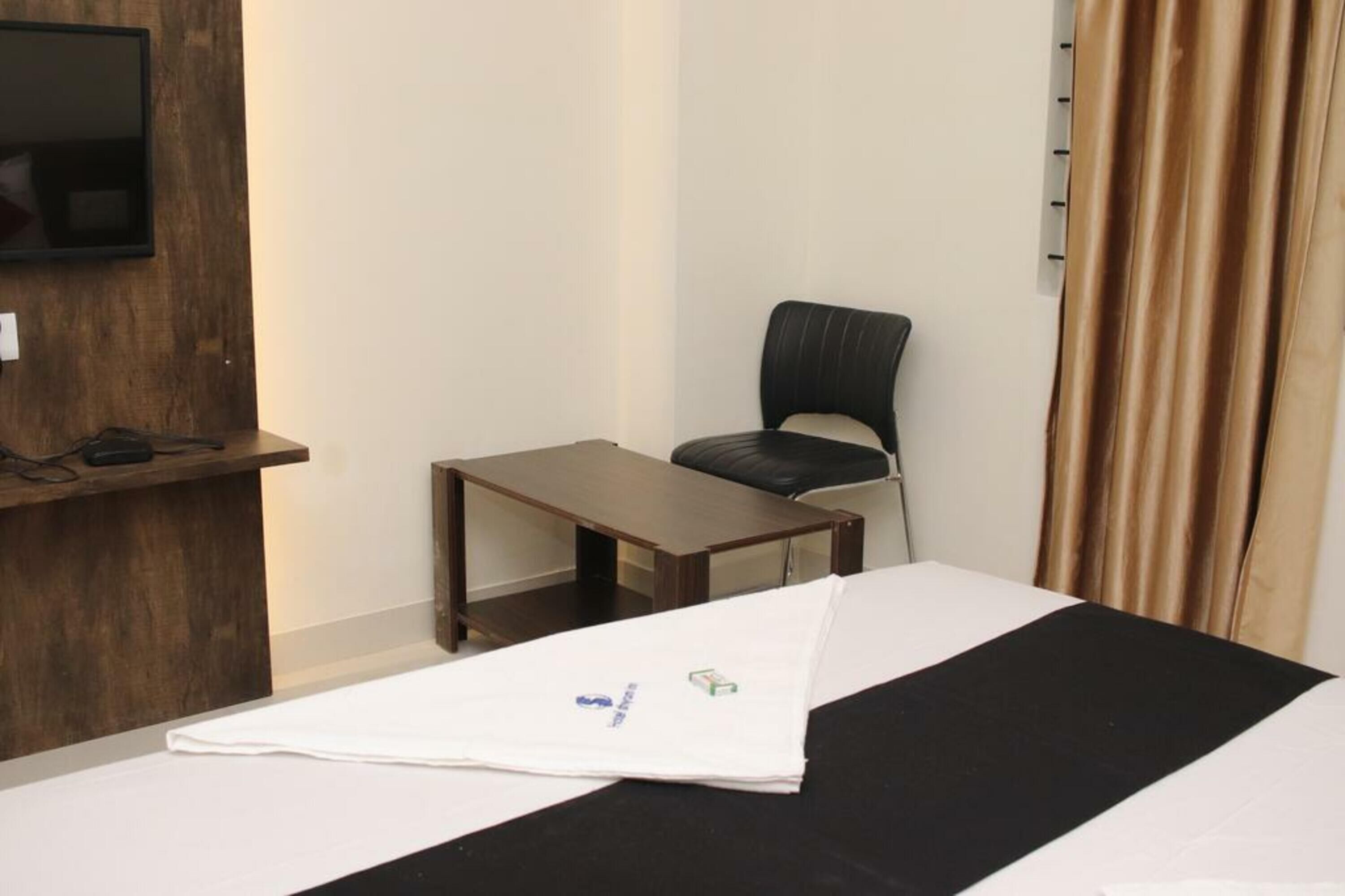 A hotel room with a bed, a small table, a chair, a TV mounted on the wall, and a curtain.