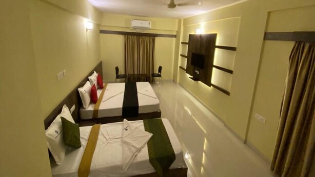 A hotel room with two beds, a flat-screen TV mounted on the wall, a ceiling fan, and an air conditioning unit. - Hotel Shyam Inn (Bengaluru)