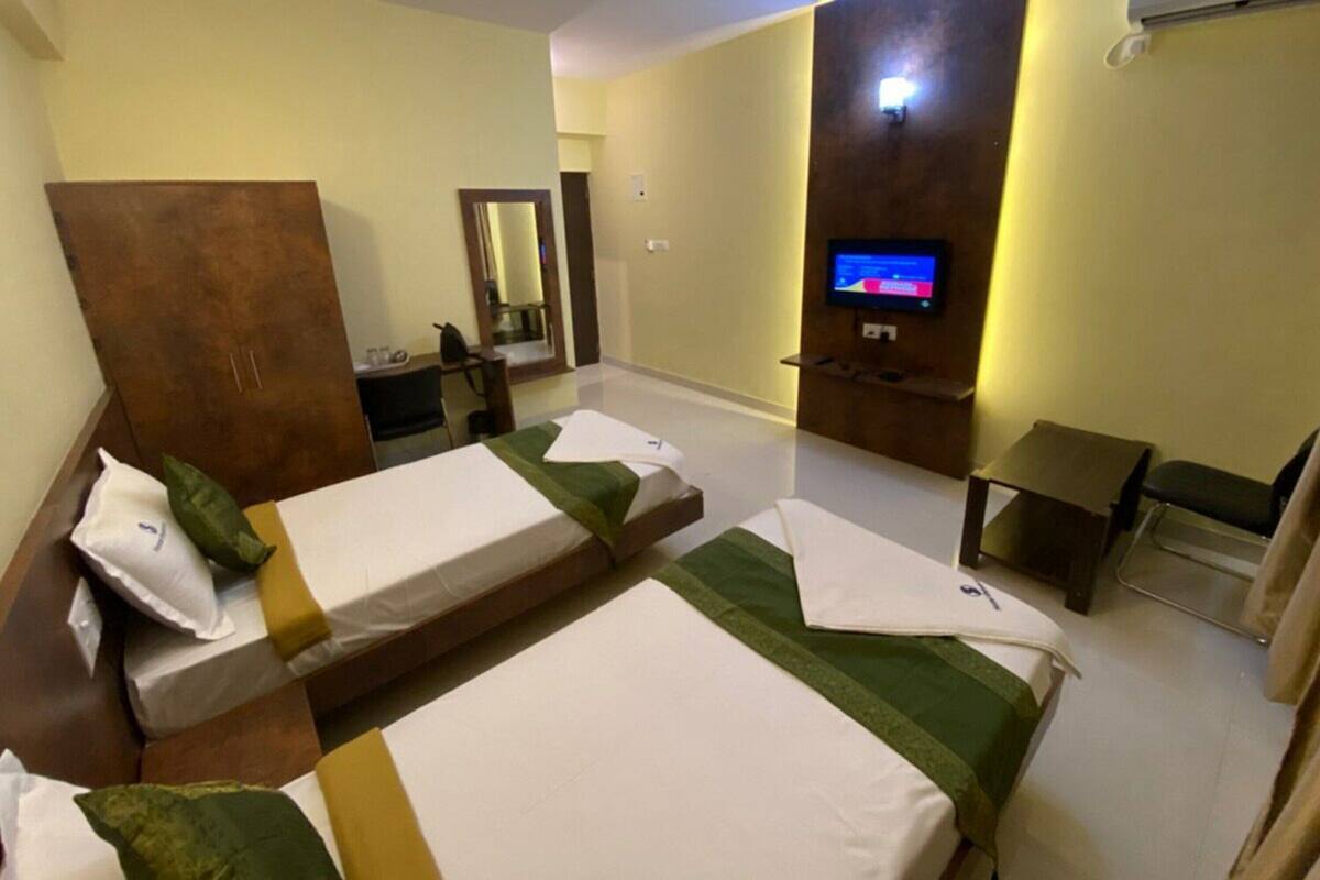 A hotel room with two single beds, a desk, a chair, a TV, and a mirror.