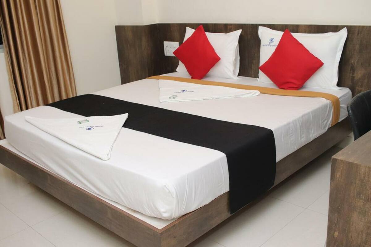 A hotel room with a bed, a wooden headboard, a black and white bedspread, and red pillows.