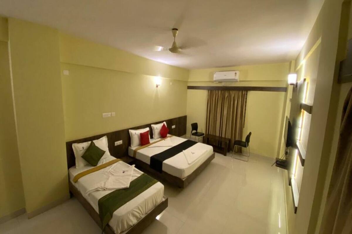 A hotel room with two beds, a desk, a chair, and a ceiling fan.