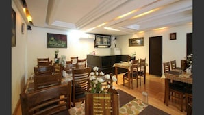 A dining area with wooden furniture, a reception desk, and a television. - Hotel Shyam Inn (Bengaluru)