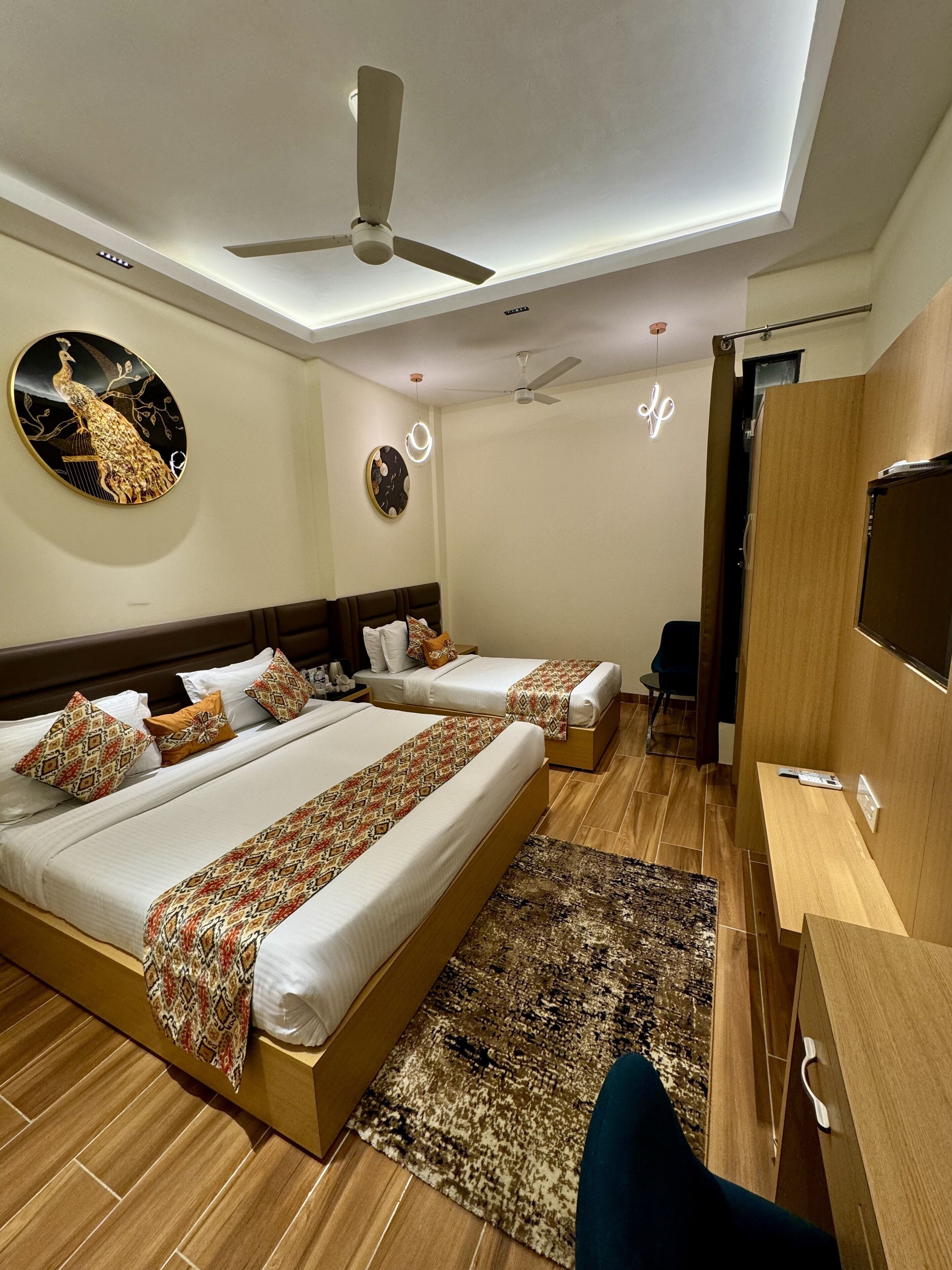A hotel room with two beds, a ceiling fan, a TV, and a desk.