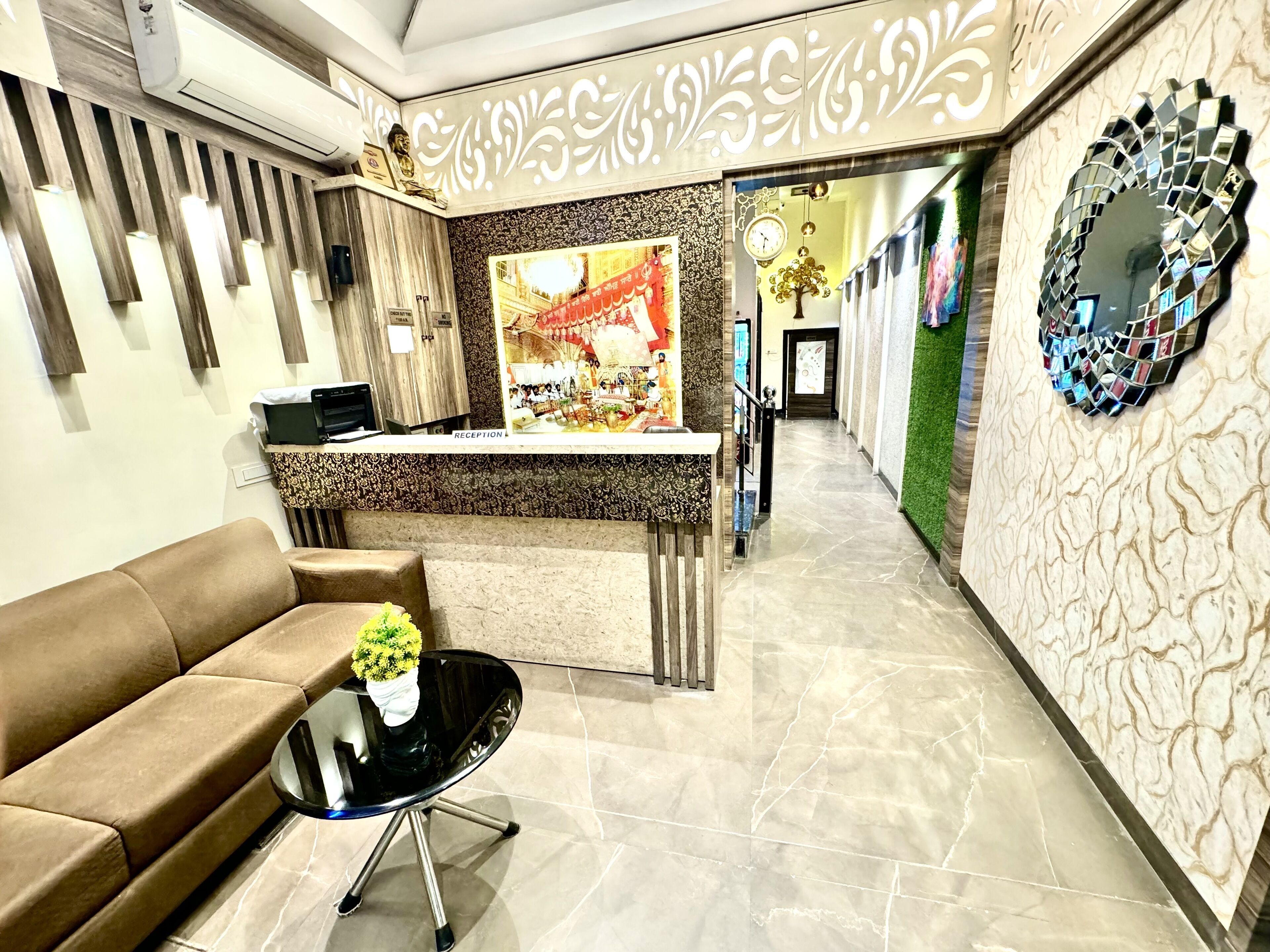 A reception area with a reception desk, a brown sofa, a small table with a plant, and a decorative wall with a clock and mirror.