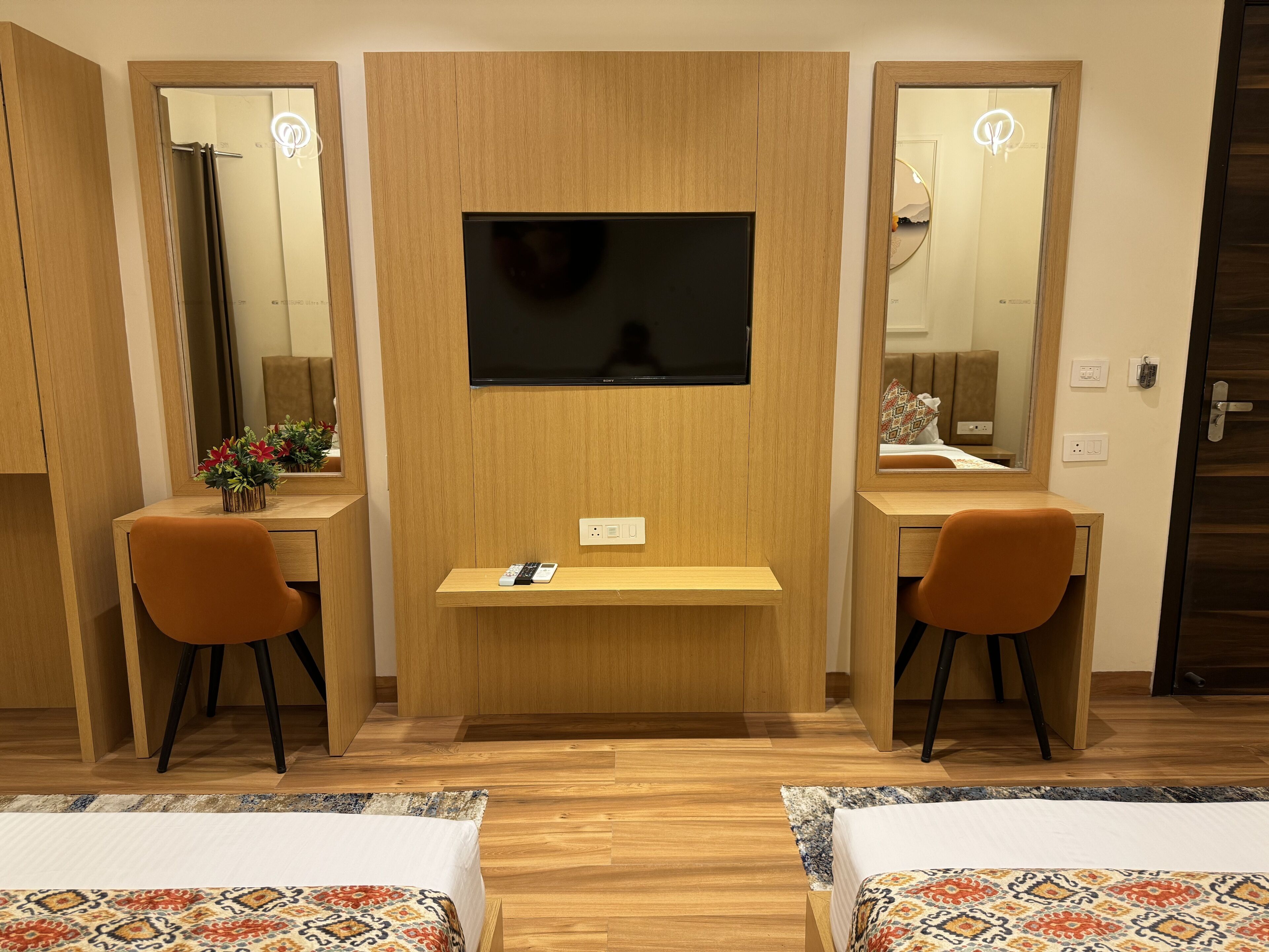 Une chambre d’hôtel avec un bureau en bois, deux chaises, une télévision et deux lits.