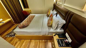 A hotel room with a bed, a desk, a chair, a nightstand, and a bedside table.