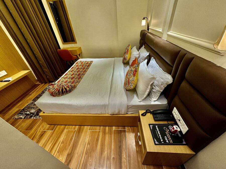 A hotel room with a bed, a desk, a chair, a nightstand, and a bedside table.